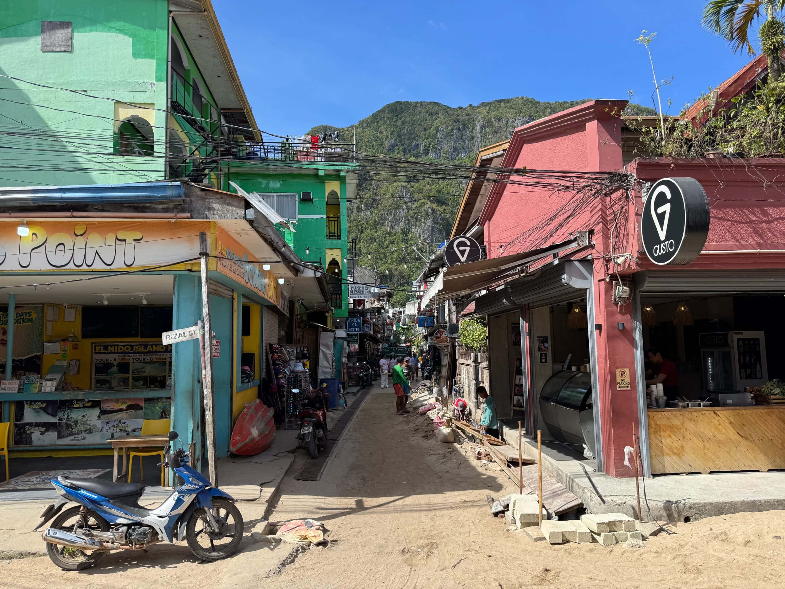 Colourful street in El Nido town with shops, cafes, and mountains in the background, showing the compact and walkable layout