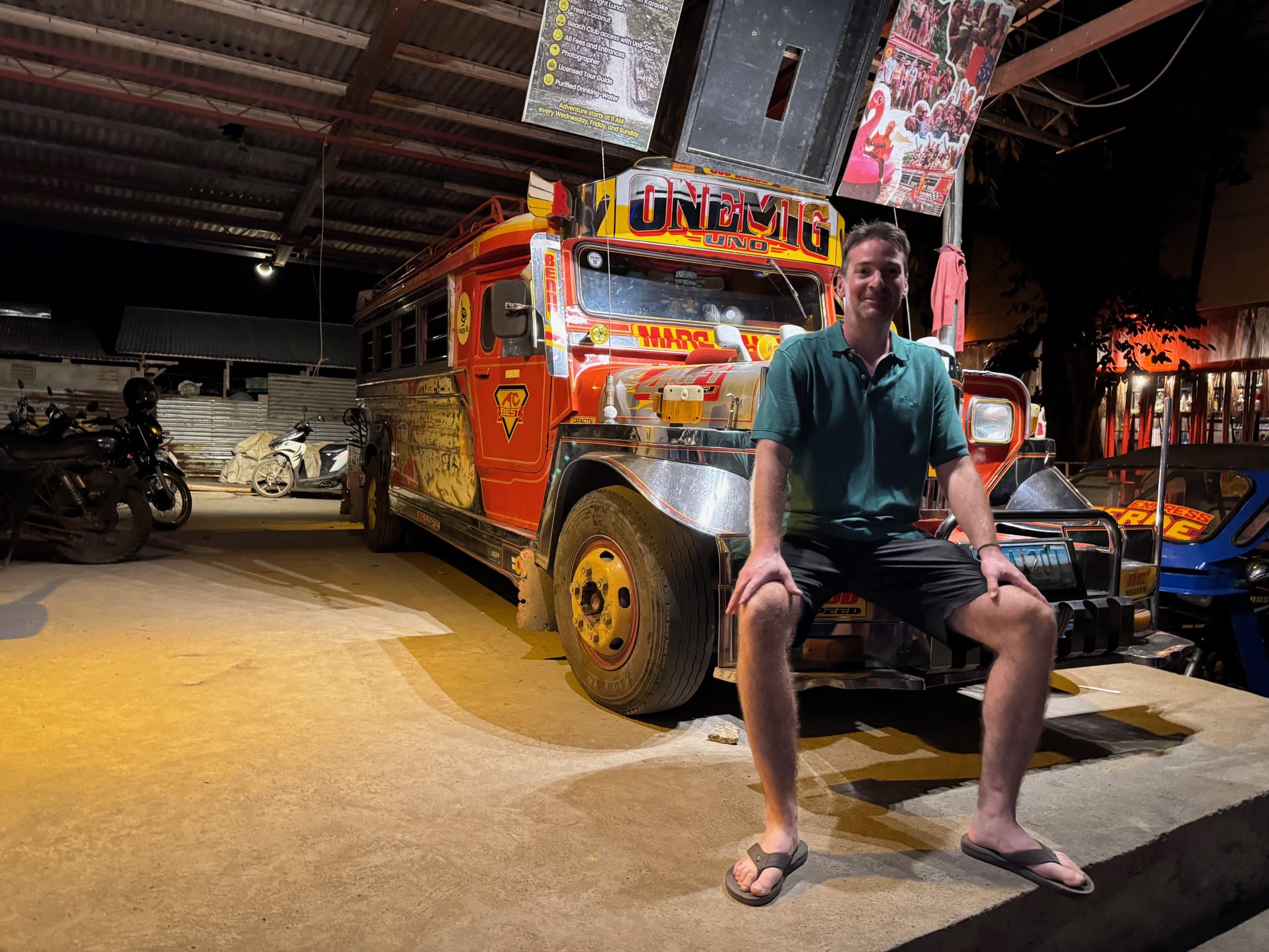 Smiling traveller sitting on a colourful jeepney in El Nido at night, showcasing classic local transport and Filipino culture in Palawan