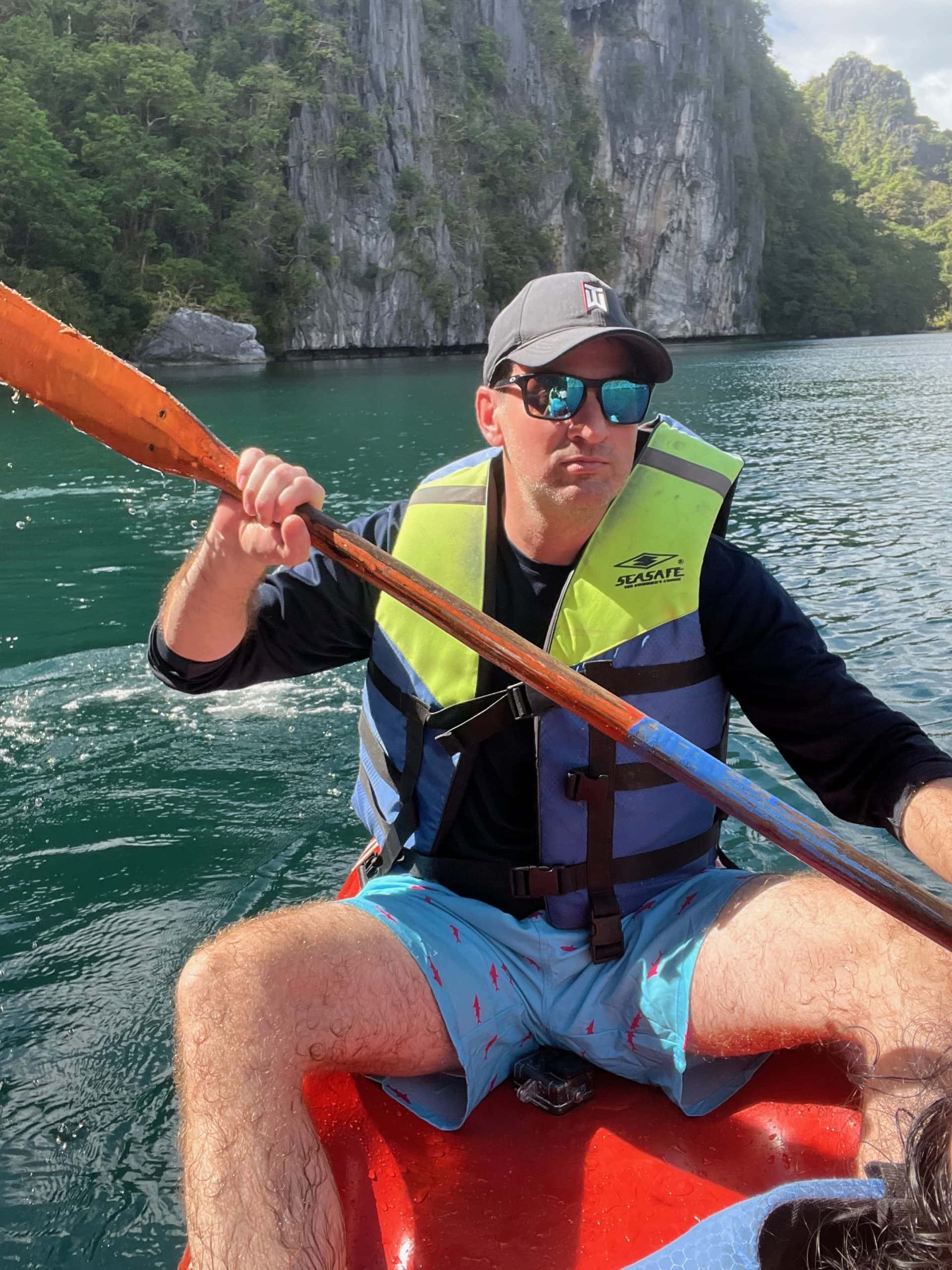 Kayaking through crystal clear lagoon waters in El Nido with towering limestone cliffs and lush jungle scenery in Palawan Philippines
