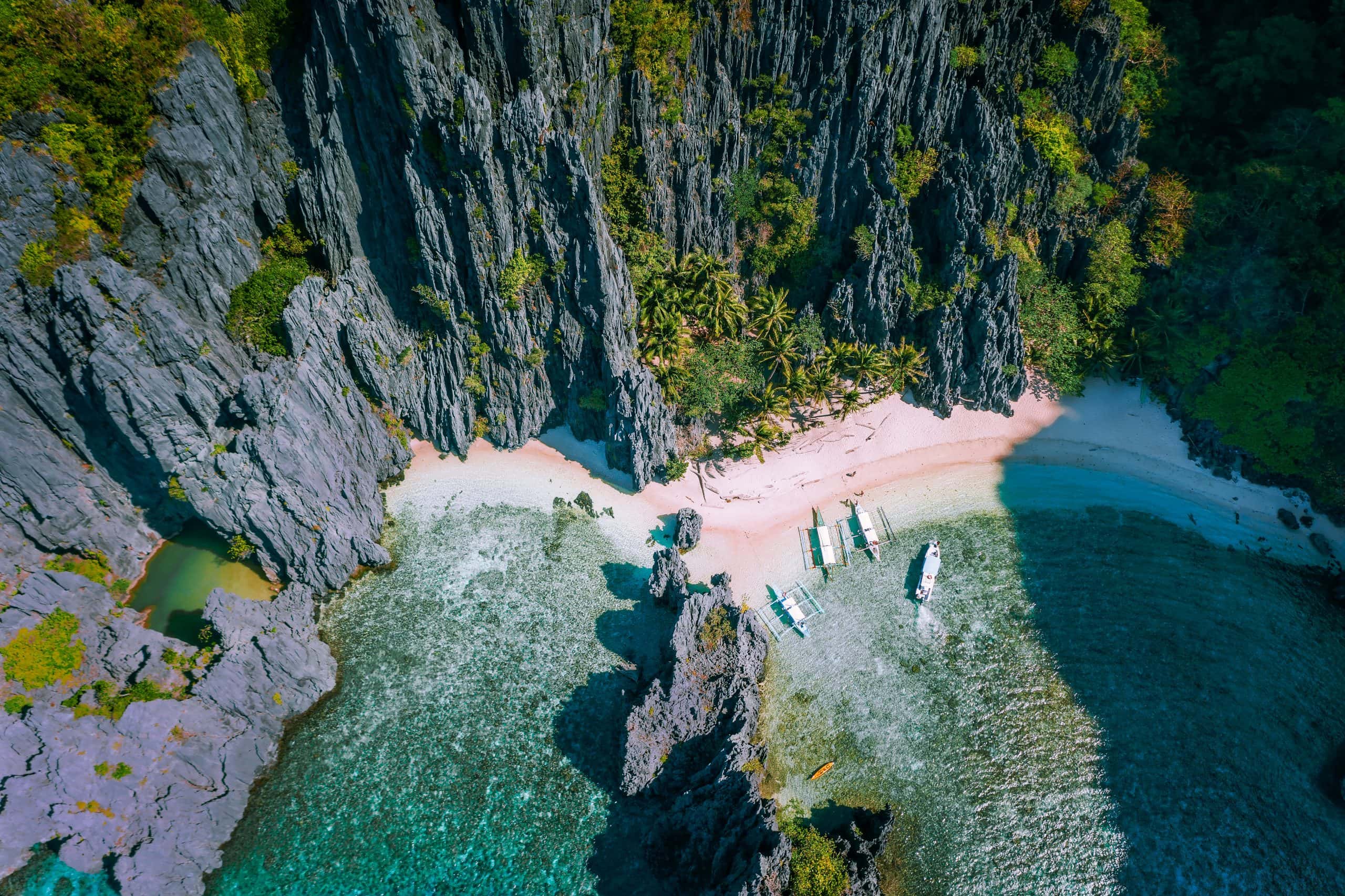 Aerial view of a hidden El Nido beach surrounded by dramatic limestone cliffs and crystal clear turquoise water with traditional boats anchored along the shore in Palawan Philippines