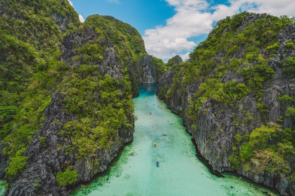 Aerial view of Big Lagoon in El Nido with turquoise water kayaks and towering limestone cliffs in Palawan Philippines.