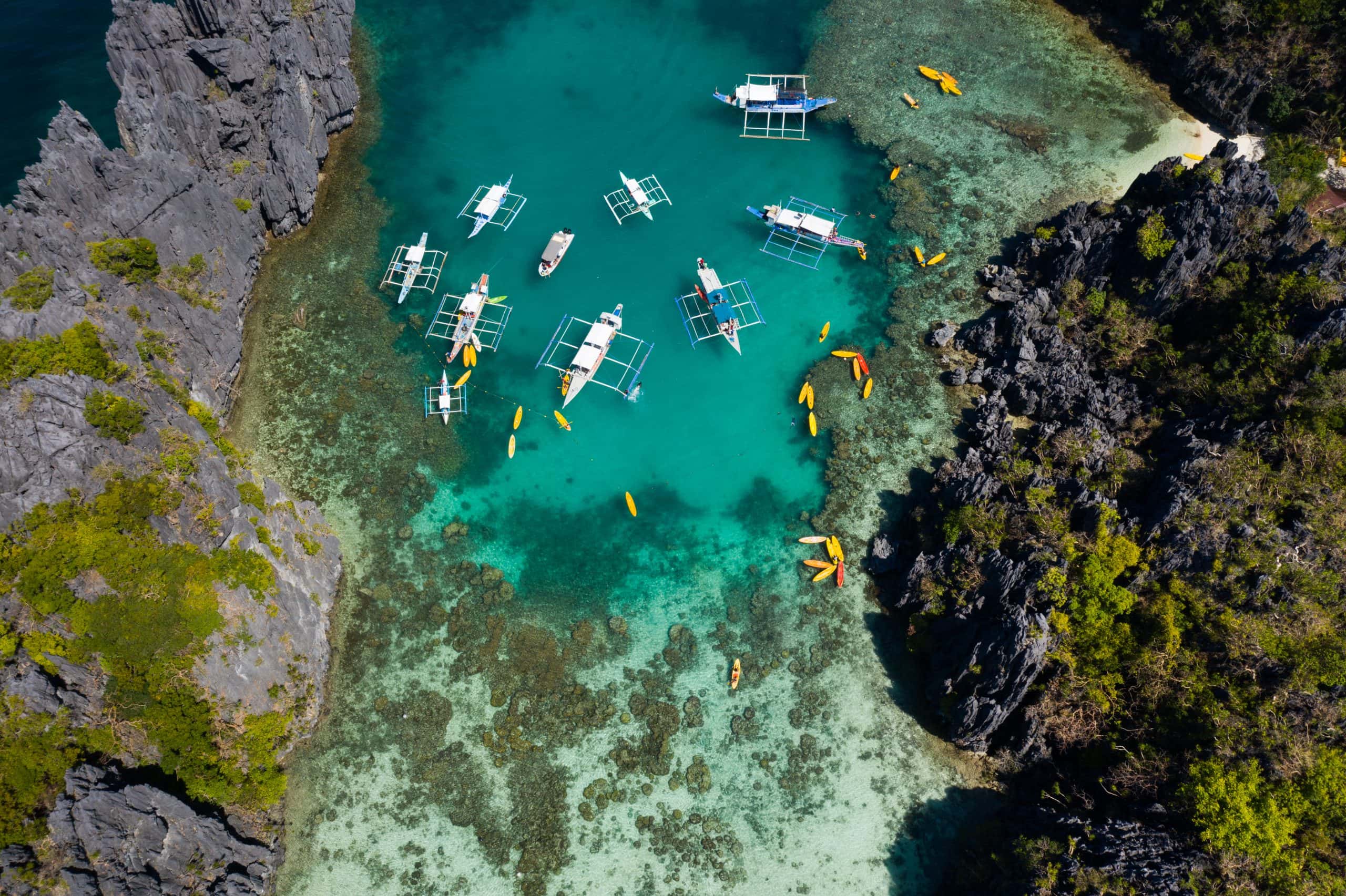 Aerial view of El Nido lagoon with traditional boats and kayaks in clear turquoise water surrounded by limestone cliffs in Palawan Philippines