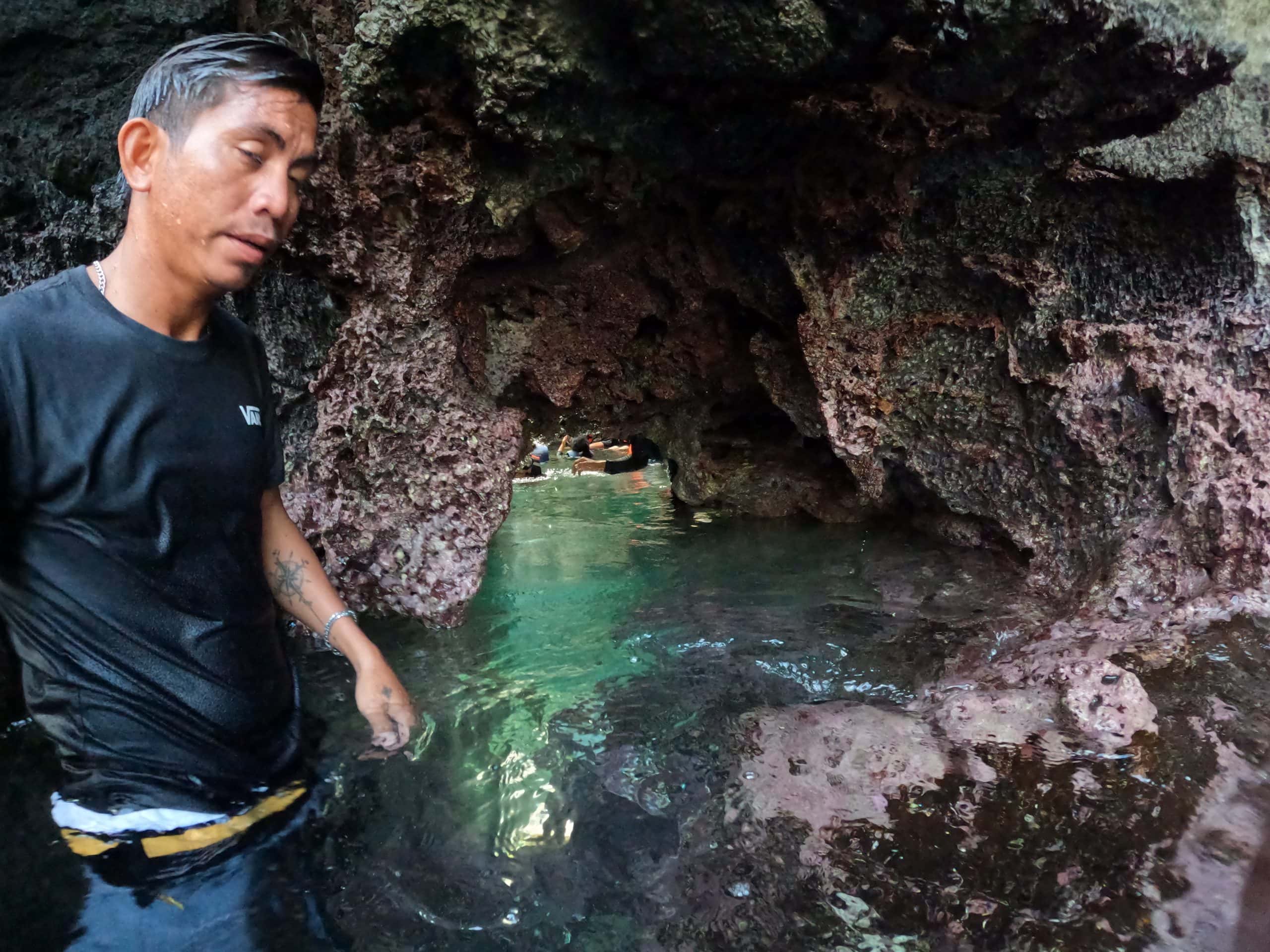 Swimming through the narrow limestone opening into Secret Lagoon during El Nido island hopping Tour A in Palawan, Philippines.