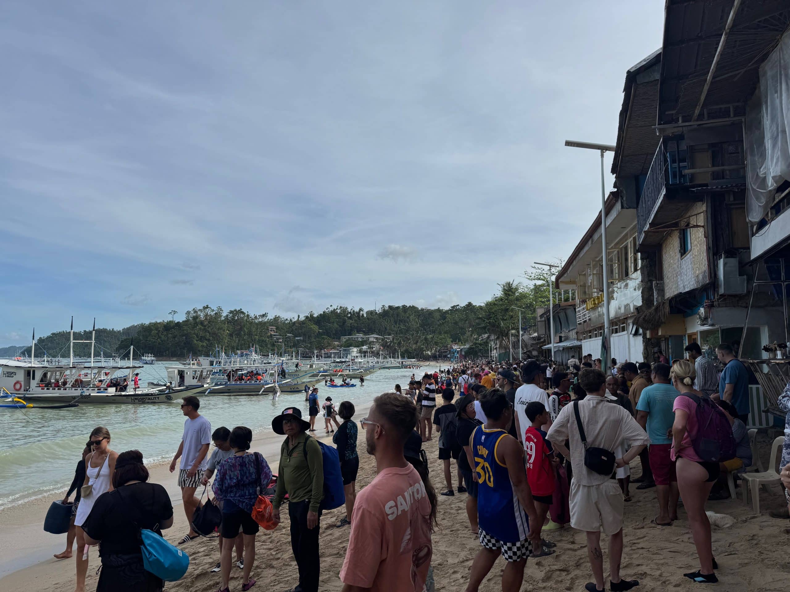 Crowds gathering on the beach in El Nido town before island hopping tours with traditional boats lining the shore in Palawan Philippines.
