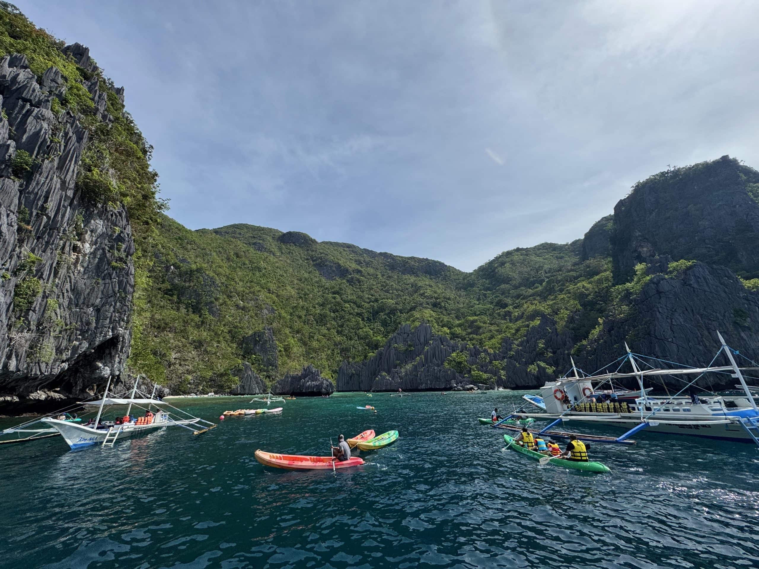 Kayaking and island hopping boats inside Big Lagoon during El Nido Tour A in Palawan, Philippines, surrounded by towering limestone cliffs and turquoise water.