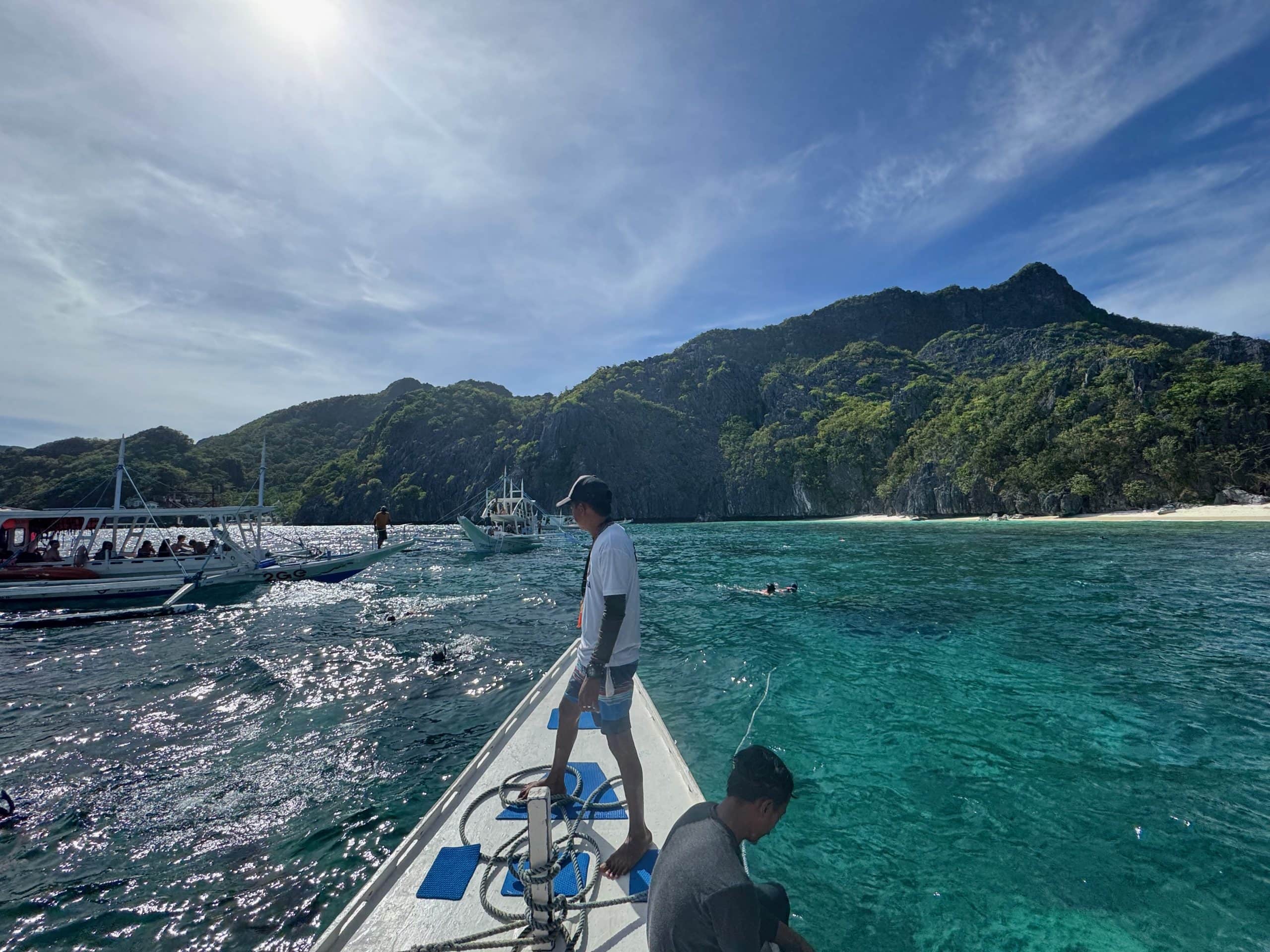 Tour boat floating in turquoise water during El Nido Tour C in Palawan, Philippines, with limestone cliffs and white sand beaches in the background.