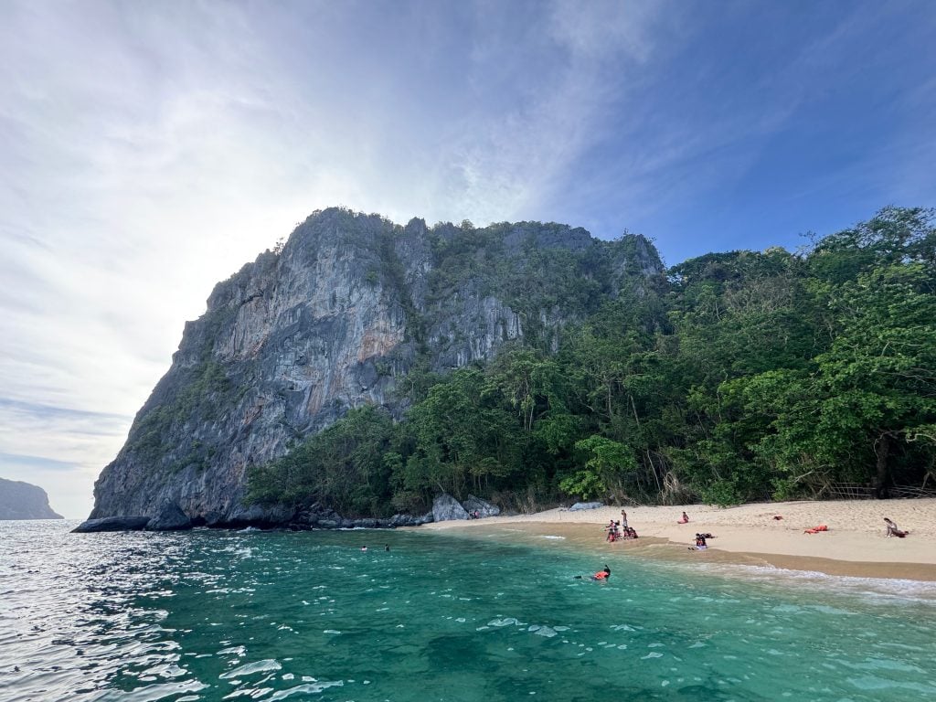 White sand beach and towering limestone cliffs at Helicopter Island during El Nido Tour C island hopping in Palawan, Philippines.