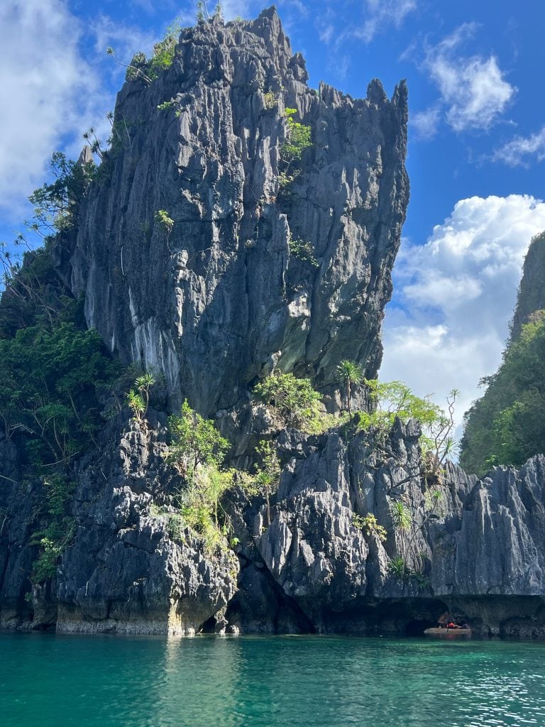 Towering limestone cliffs rising above crystal clear turquoise water during an island hopping tour in El Nido, Palawan, Philippines.