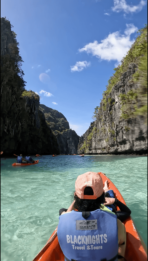 Kayaking through Big Lagoon in El Nido surrounded by crystal clear turquoise water and towering limestone cliffs in Palawan Philippines.