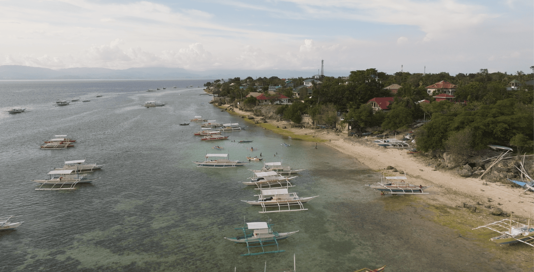 Aerial view of Moalboal, Cebu, showing the coastline near Panagsama Beach with traditional Filipino boats, clear turquoise water, and one of the Philippines’ top diving destinations.