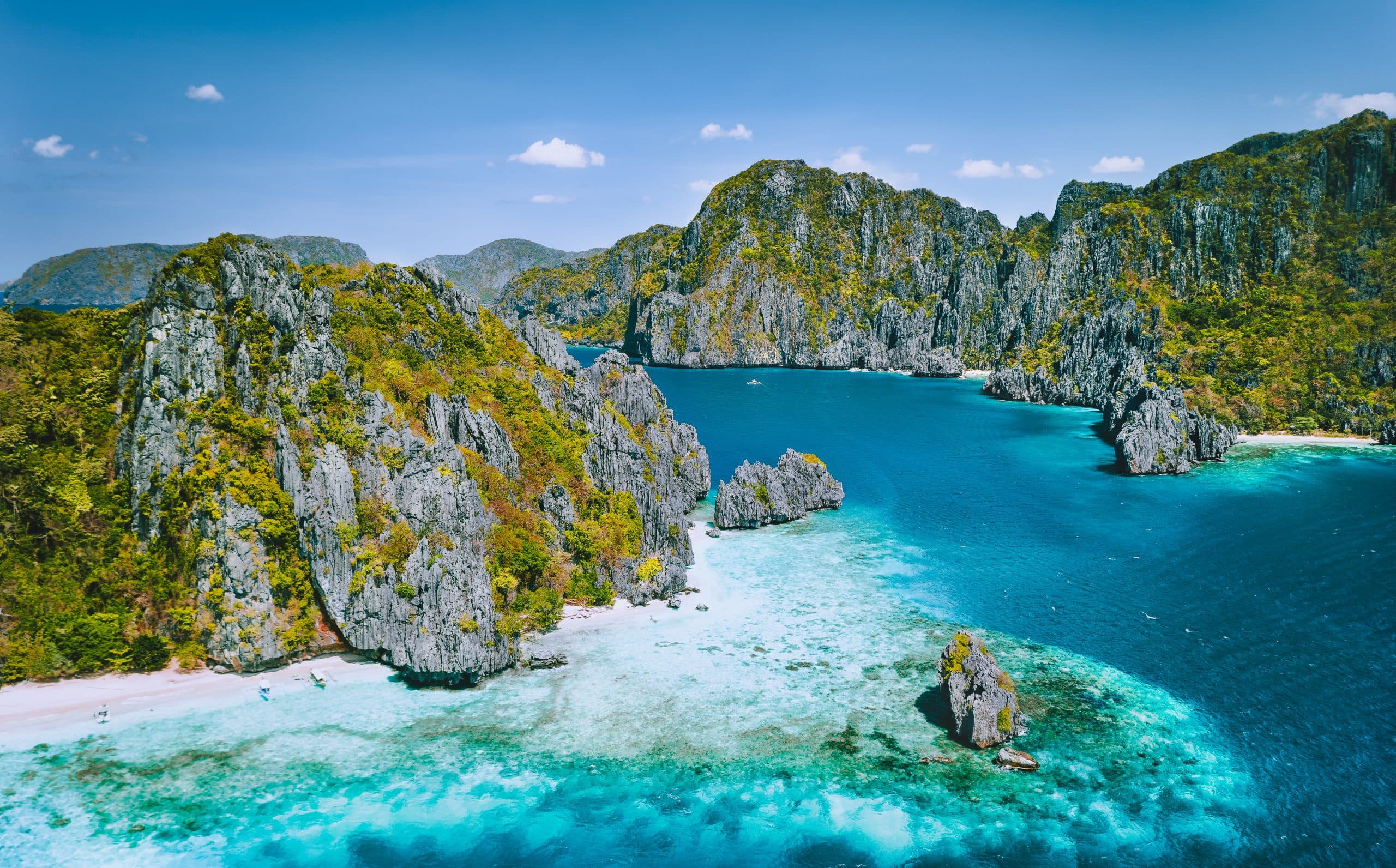 El Nido, Palawan, Philippines. Aerial view of tropical Island with tourist boats moored at white sandy beach. Jugged karst limestone sea stack mountain cliffs. Bacuit archipelago.