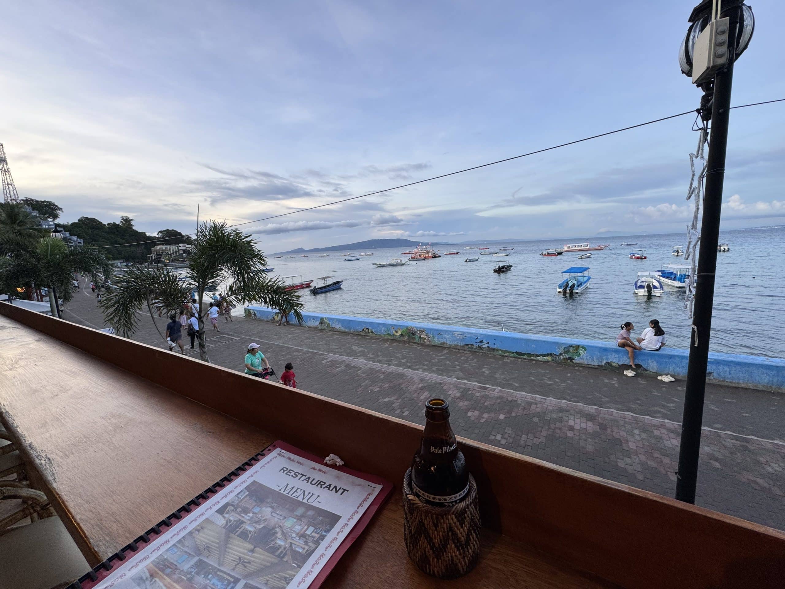 Waterfront view in Puerto Galera, Mindoro, with boats in the bay and the seaside promenade at sunset.