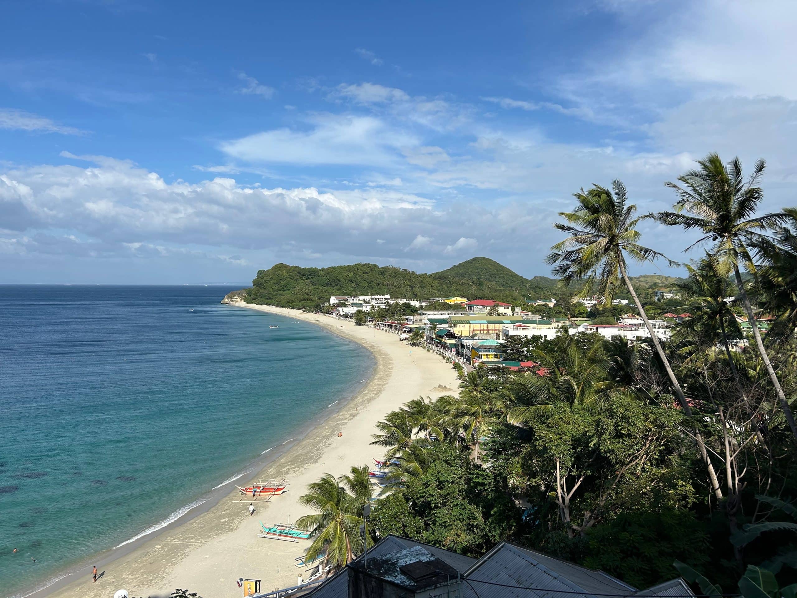 Puerto Galera White Beach: White Beach in Puerto Galera, Mindoro, with clear blue water, palm trees and beachfront resorts along the coast.