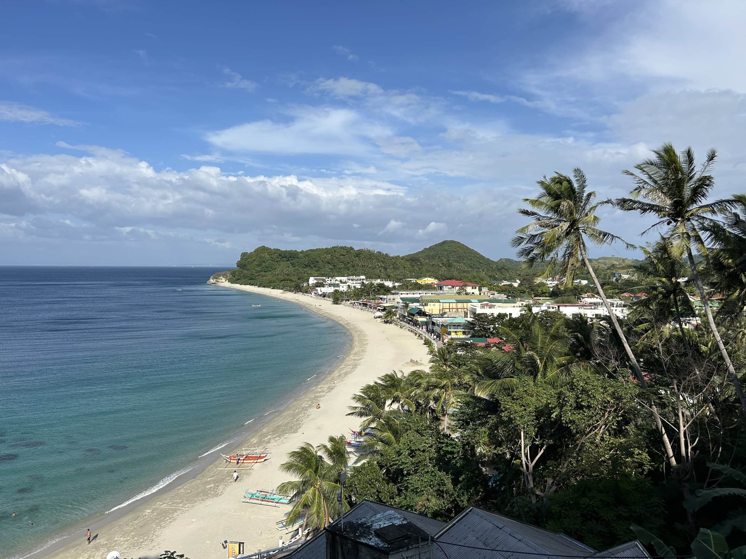White Beach in Puerto Galera, Mindoro, with its long sandy shoreline, clear blue water, palm trees and beachfront town.