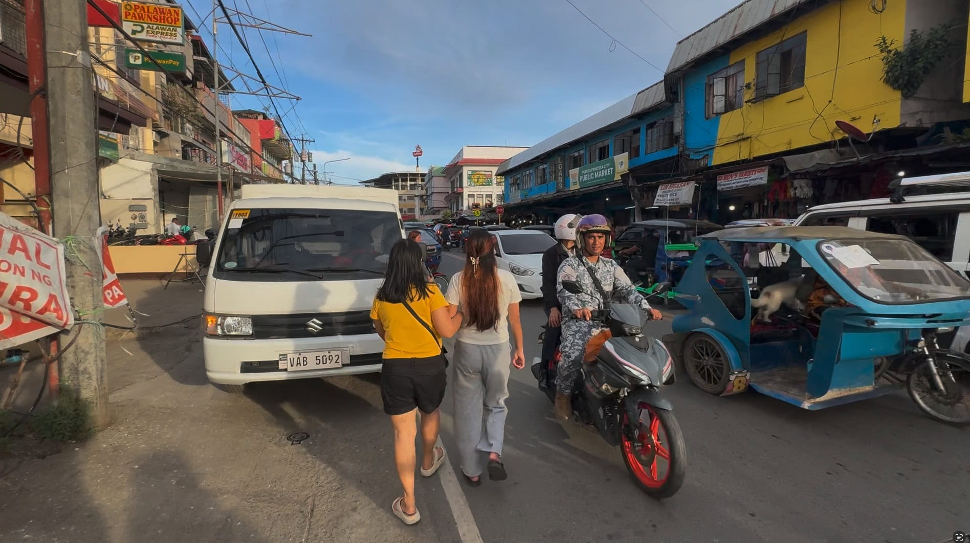 Busy street traffic in Puerto Princesa, Palawan, showing pedestrians sharing the road with motorcycles, vans and tricycles.