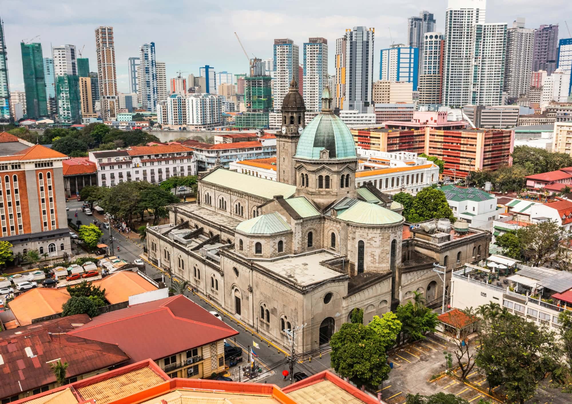 Aerial view of Manila Cathedral with the modern skyline of Makati rising in the background.