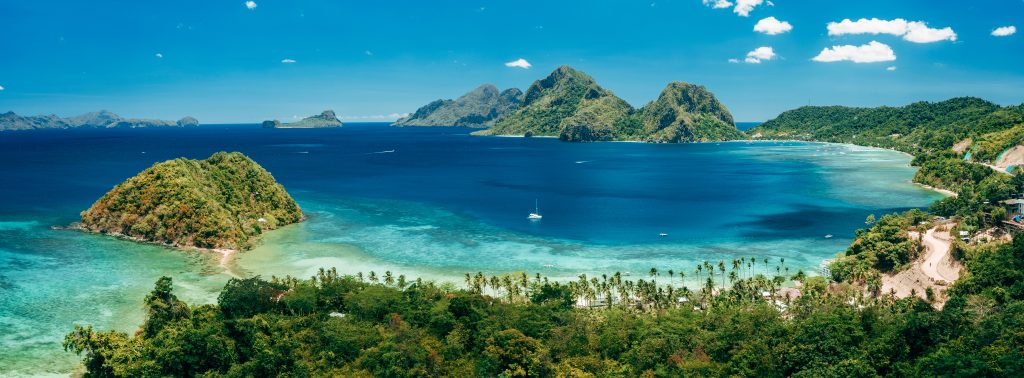 Panoramic view of Las Cabanas Beach in El Nido, Palawan, Philippines, with turquoise water, tropical islands and lush green coastline.