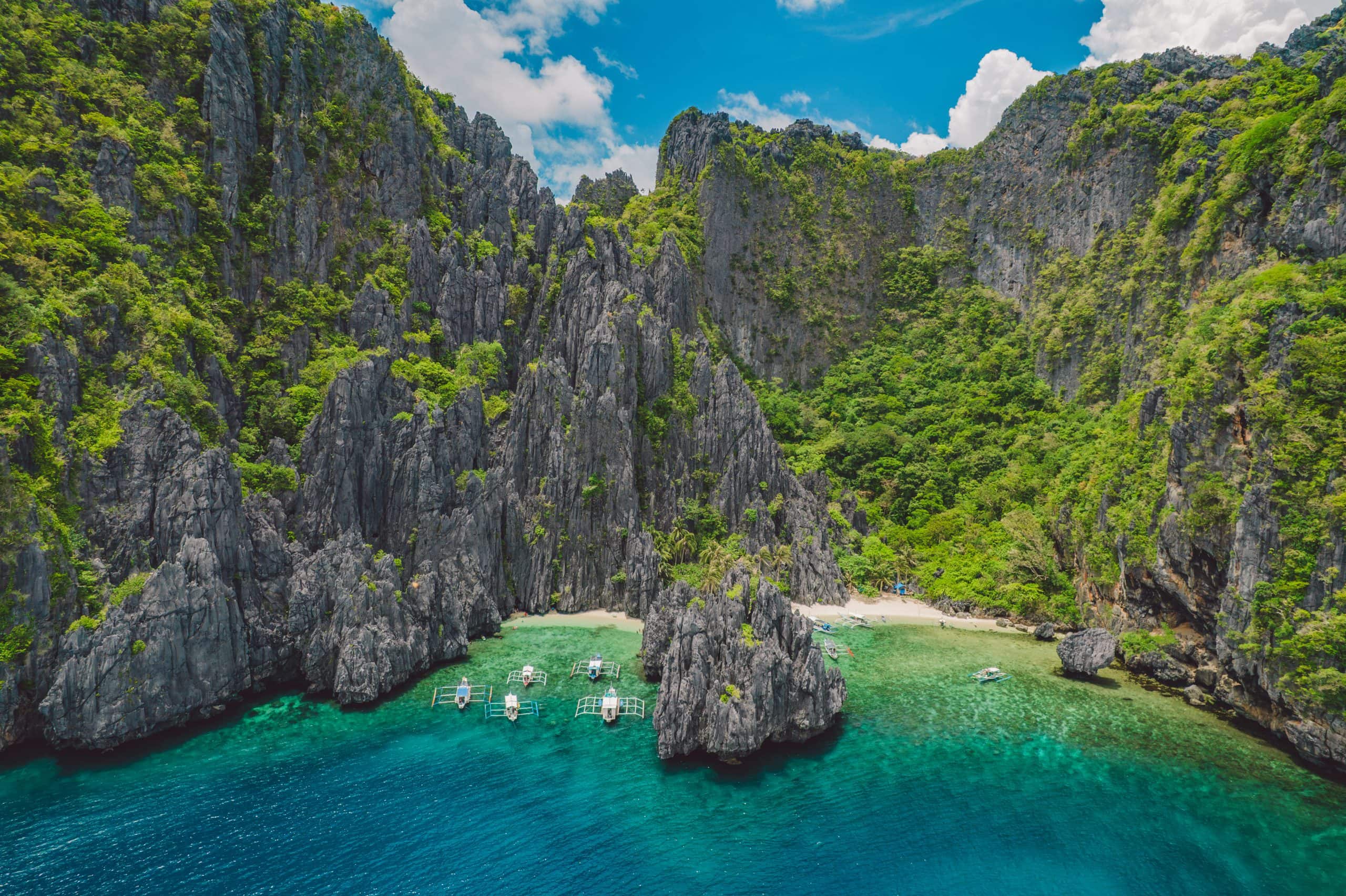Dramatic limestone cliffs, turquoise water and traditional boats along the tropical coastline of El Nido, Palawan, Philippines.