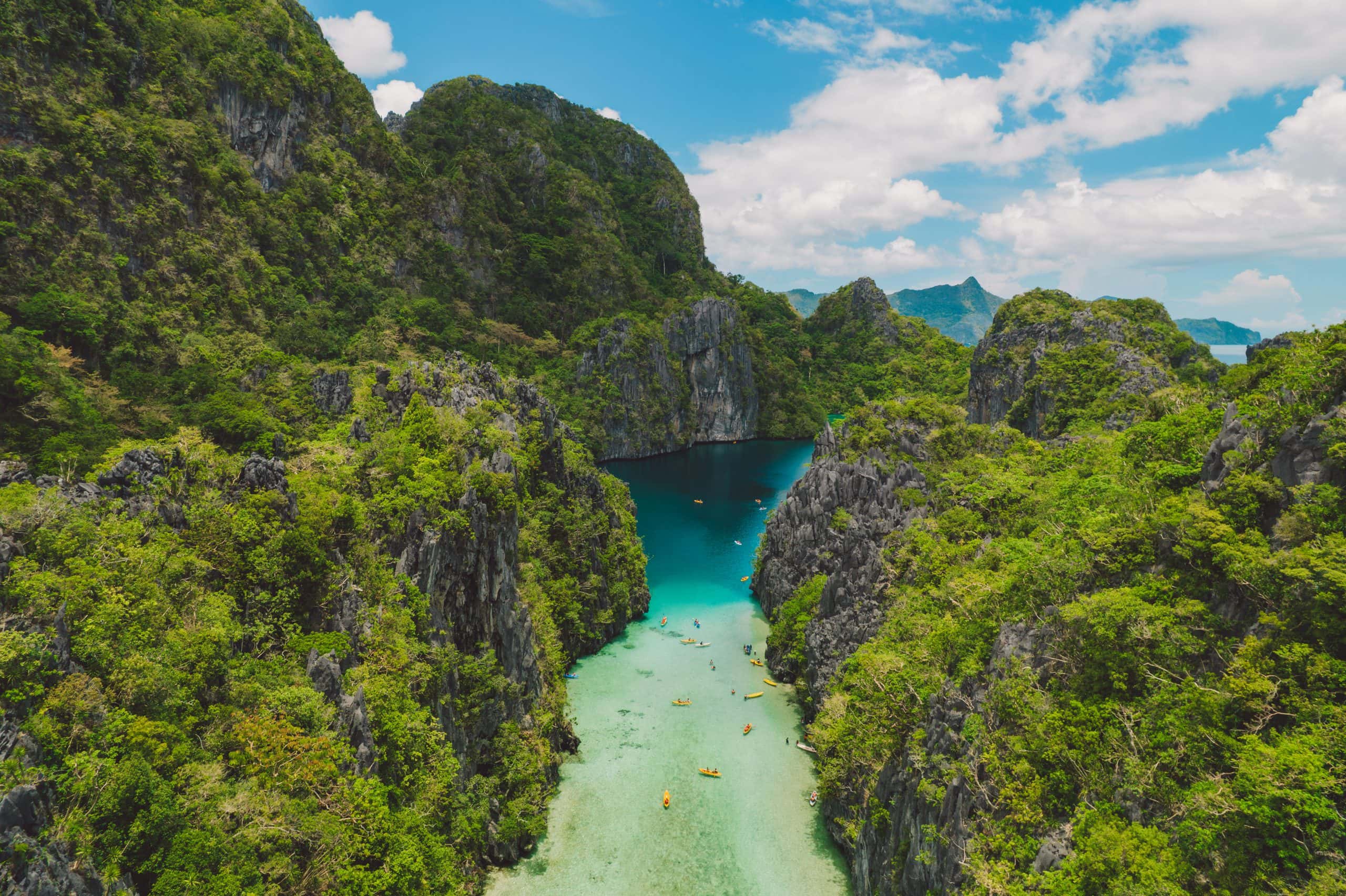 Aerial view of a turquoise lagoon surrounded by dramatic limestone cliffs and lush tropical scenery in El Nido, Palawan, Philippines.